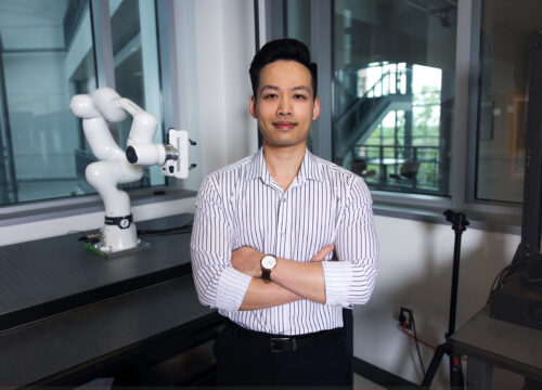 Professor stands with arms crossed in robotics lab.