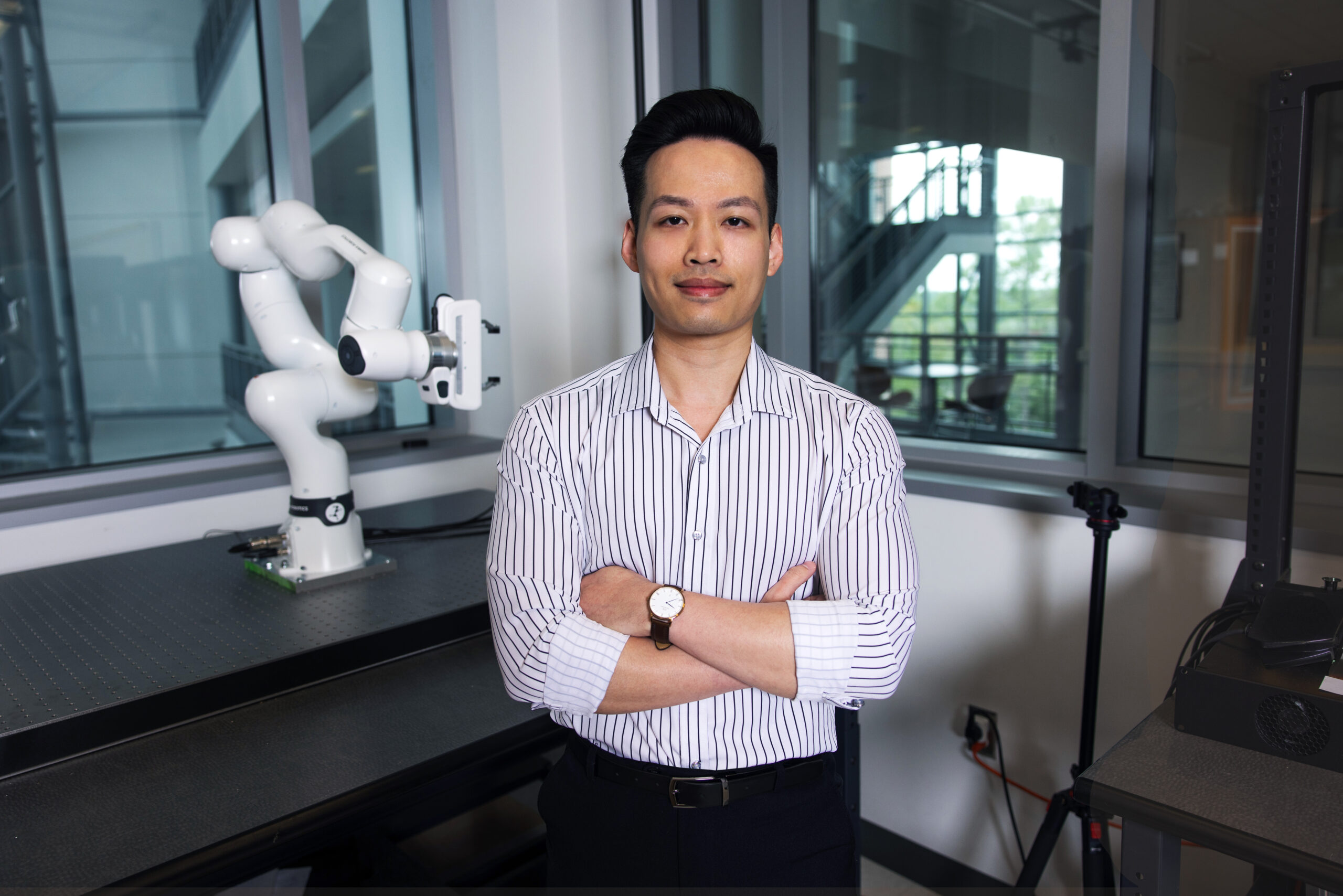 Professor stands with arms crossed in robotics lab.