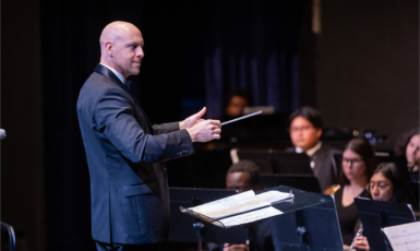 Standing conductor directs seated symphonic band.