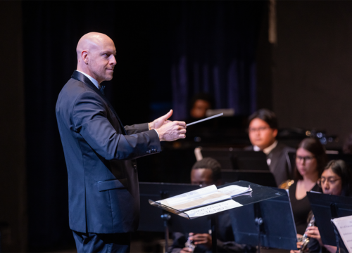 Standing conductor directs seated symphonic band.