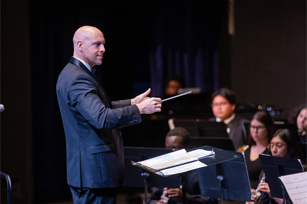Standing conductor directs seated symphonic band.